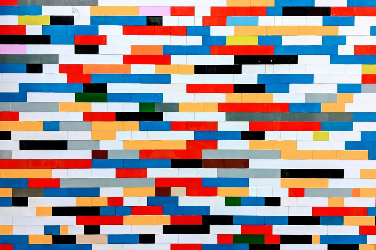 A vibrant mosaic wall constructed from Lego bricks in a spectrum of colors including red, blue, white, yellow, and black, arranged in a modern, geometric pattern